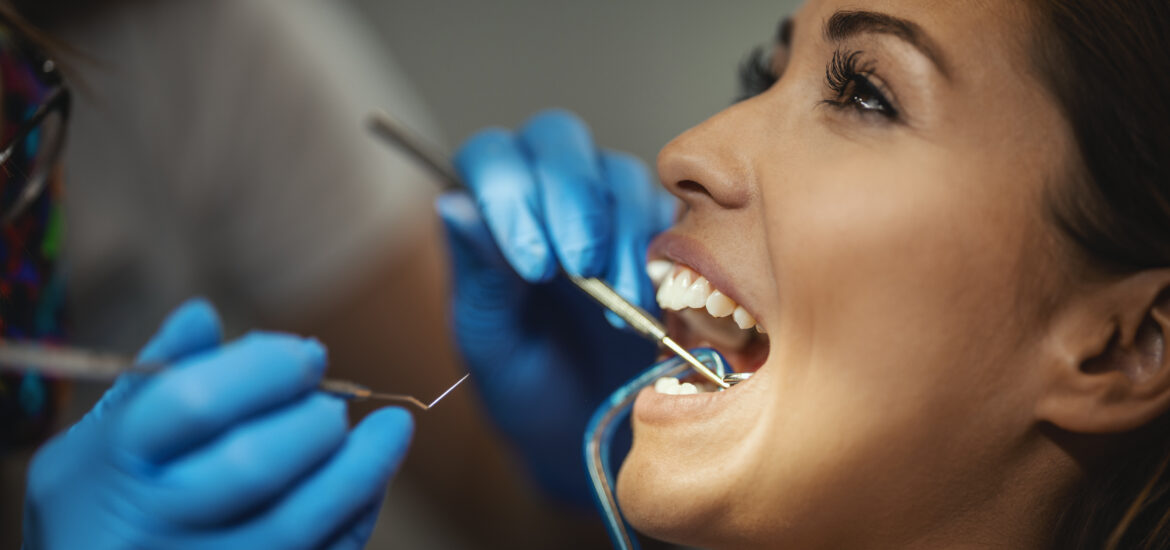 young woman in dental chair having her teeth examined by a doctor in blue gloves