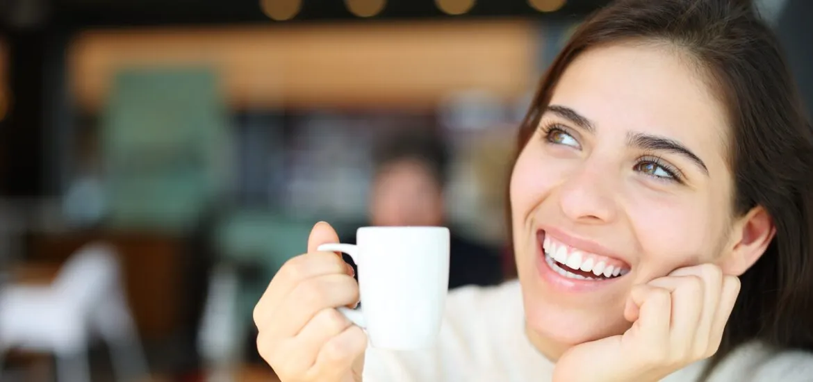 young woman smiling drinking a coffee, perfect white teeth