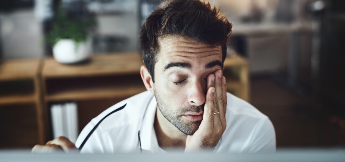 fatigued man rubbing his eyes in front of his computer