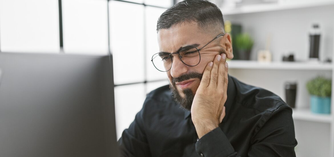 man working at his computer holding his jaw, severe tooth pain